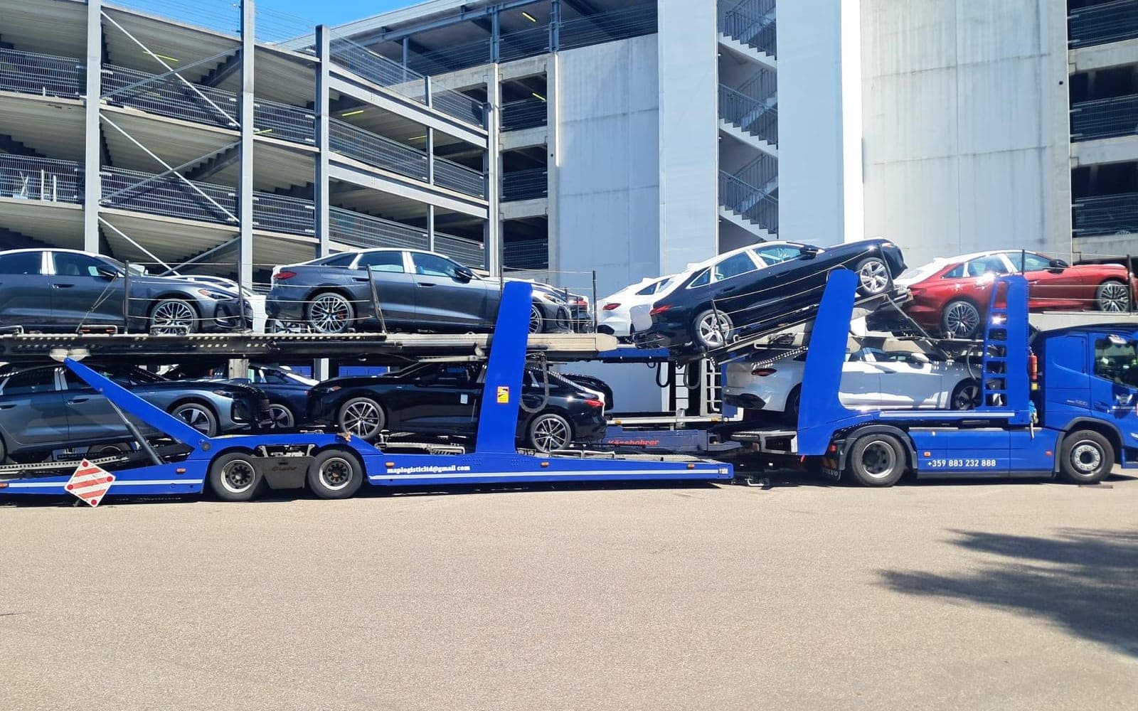 Our blue car transporter loaded with new saloon cars next to a multi-storey car park