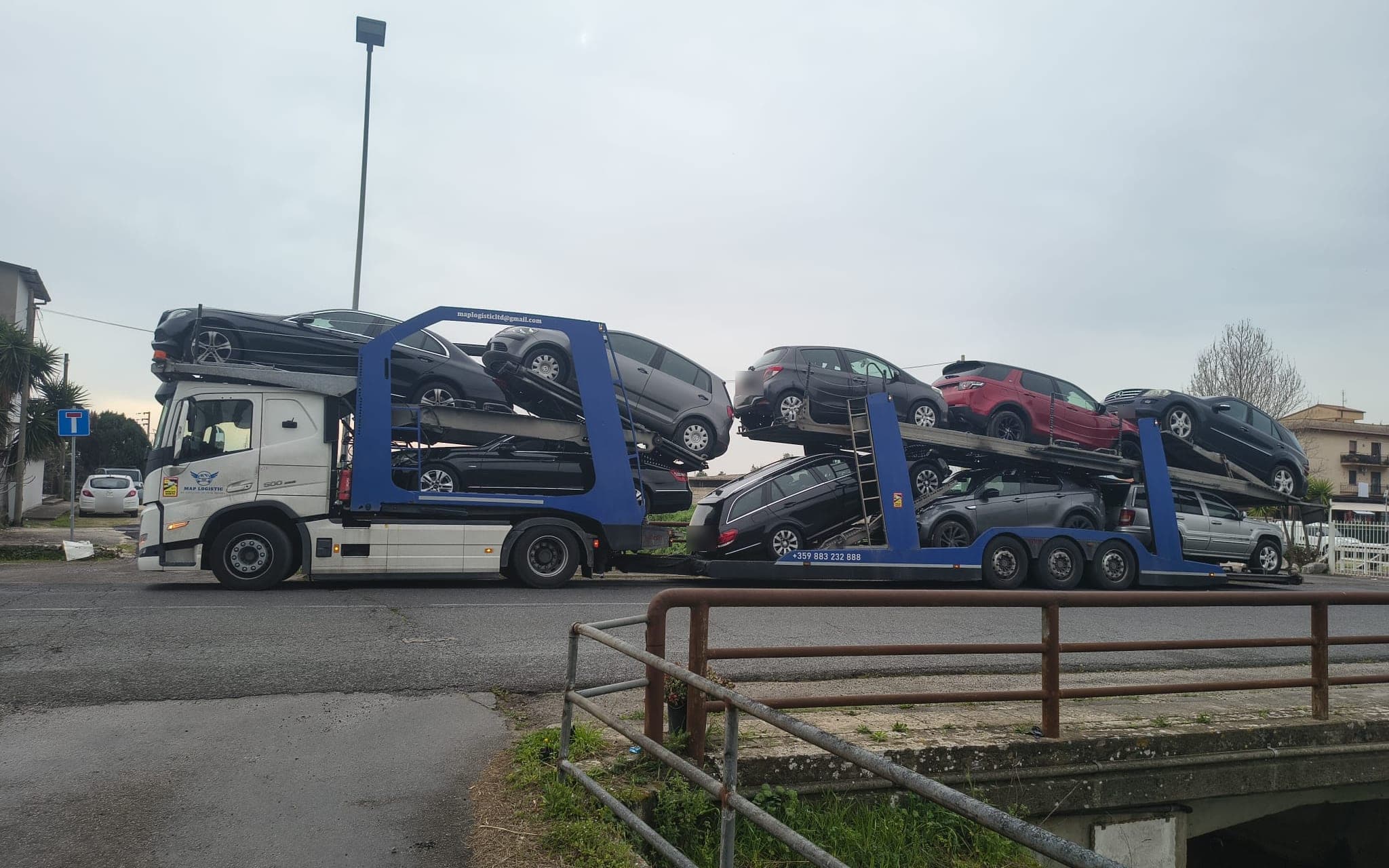 Our white truck and blue trailer loaded with used cars on a street in Italy